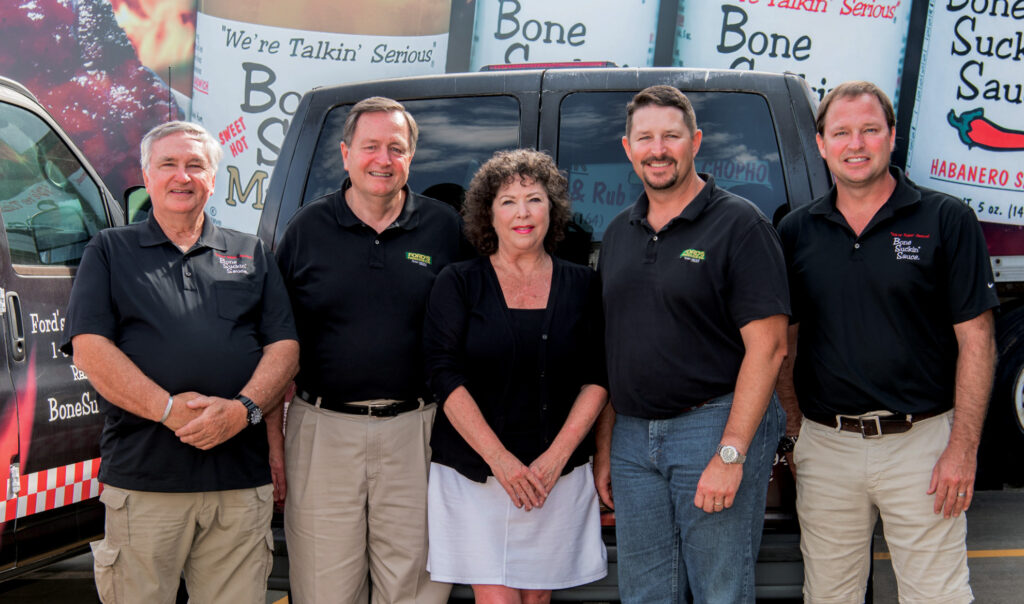 The Ford Family standing in front of a Bone Suckin' Sauce banner