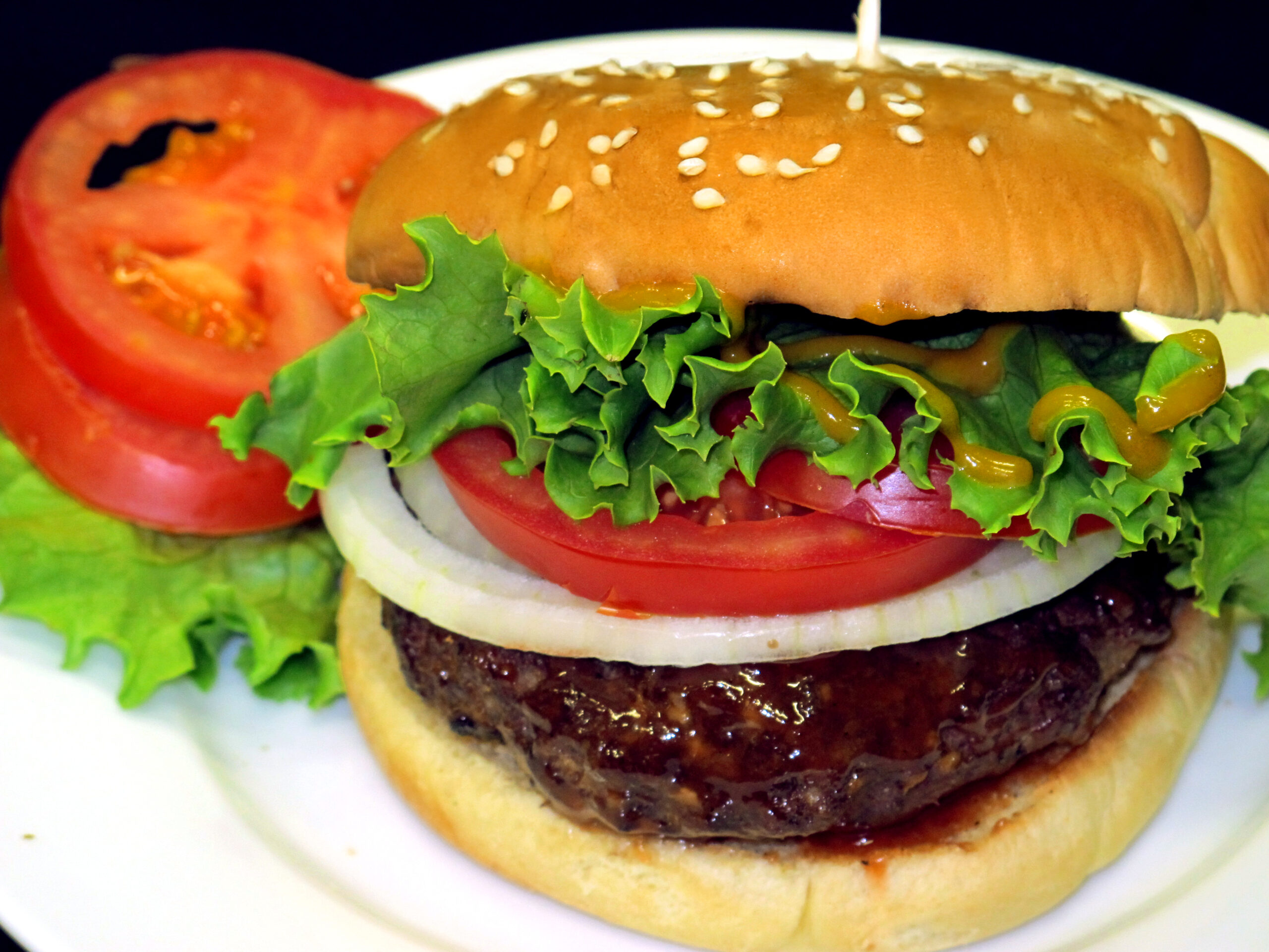 Burger with Bone Suckin Sauce and Bone Suckin' Mustard on it, with lettuce, tomato, onion